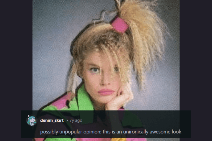  A woman with an iconic 1980s hairstyle featuring a high side ponytail secured with a large pink scrunchie, crimped and teased to perfection. She wears bold makeup with bright pink lipstick and a vibrant, oversized neon jacket with geometric patterns. A comment below praises the look, calling it “unironically awesome.”