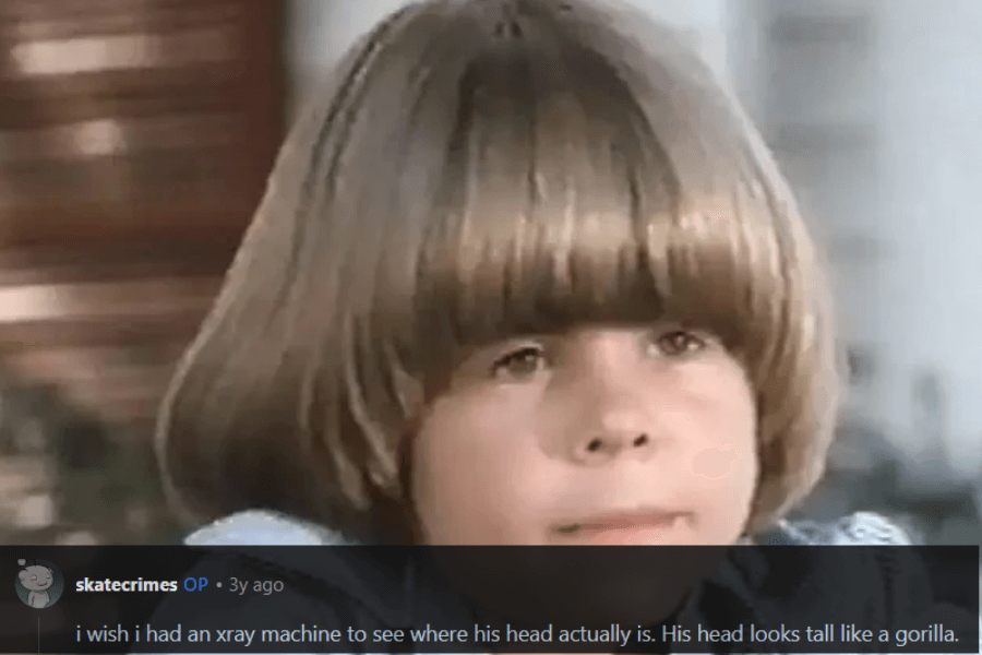 A young boy with an exaggeratedly large and perfectly rounded bowl haircut, covering most of his forehead and extending down the sides of his head. The haircut is so voluminous that it creates an almost helmet-like appearance. A humorous comment below jokes about needing an X-ray to determine where his actual head is, comparing the shape to that of a gorilla.