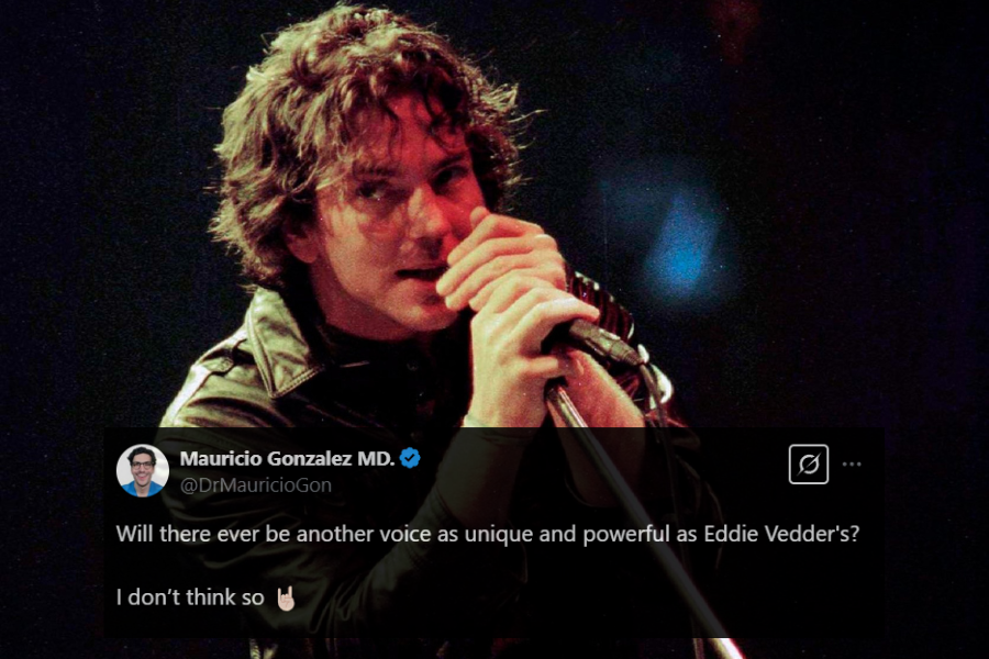 A male rock singer with tousled curly hair grips a microphone while leaning into the stand during a live performance. He wears a black leather jacket, and his intense gaze adds to the raw, emotional energy of the moment. The dim stage lighting with a subtle red glow enhances the moody and grunge-inspired atmosphere.