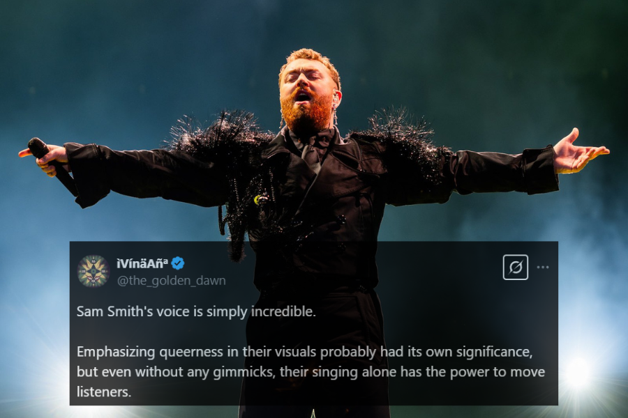 A dramatic stage photograph of a singer with a red beard, arms outstretched, passionately performing. They wear an all-black outfit adorned with shimmering feather-like embellishments on the shoulders. Bright spotlights illuminate the scene, creating a powerful and theatrical atmosphere.