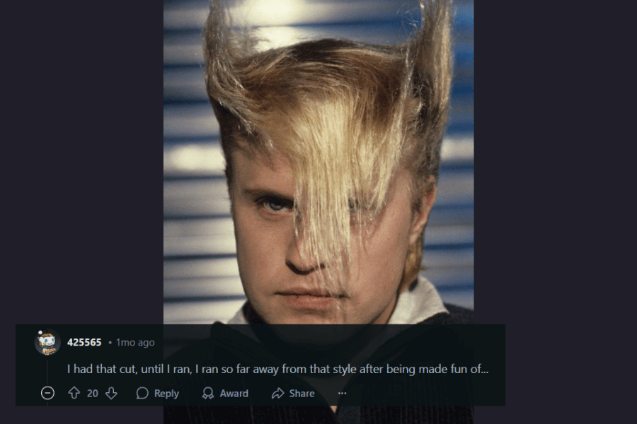 A close-up portrait of a man with an extreme 1980s hairstyle featuring sharply sculpted, upward-pointing sides and long, straight blonde bangs covering one eye. His intense expression and the dramatic lighting add to the edgy, new wave aesthetic. A comment below humorously references I Ran (So Far Away) by A Flock of Seagulls, implying they once had this hairstyle but abandoned it after being teased.