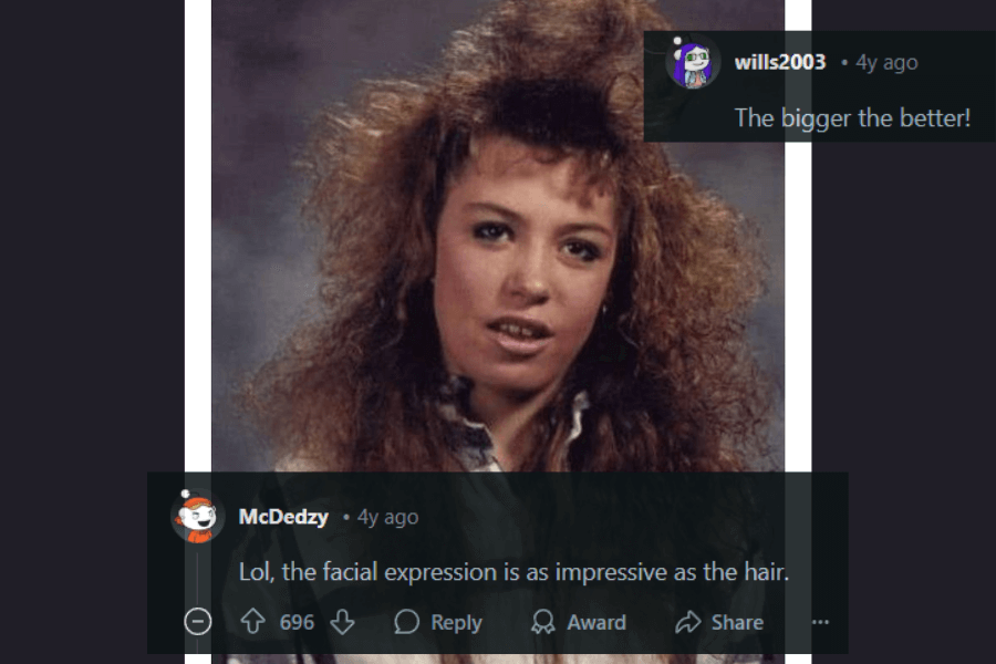 A vintage 1980s school portrait of a young woman with enormous, teased, and voluminous curly hair, reaching new heights of Aqua Net perfection. She has a confident yet slightly puzzled facial expression, adding to the charm of the era’s aesthetic. The comments below praise both the massive hair and her memorable expression, with one saying, "The bigger the better!"