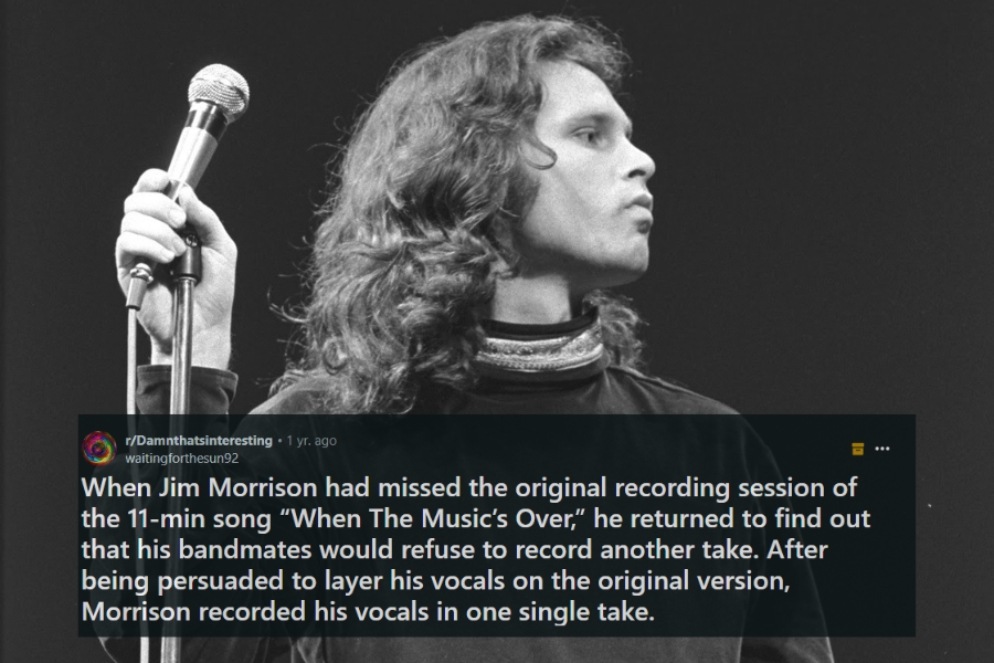 A black and white photograph of a male rock singer with wavy, shoulder-length hair standing on stage. He holds a microphone in one hand while gazing off to the side with an intense and contemplative expression. His dark, loose-fitting velvet shirt and high collar add to his enigmatic stage presence.