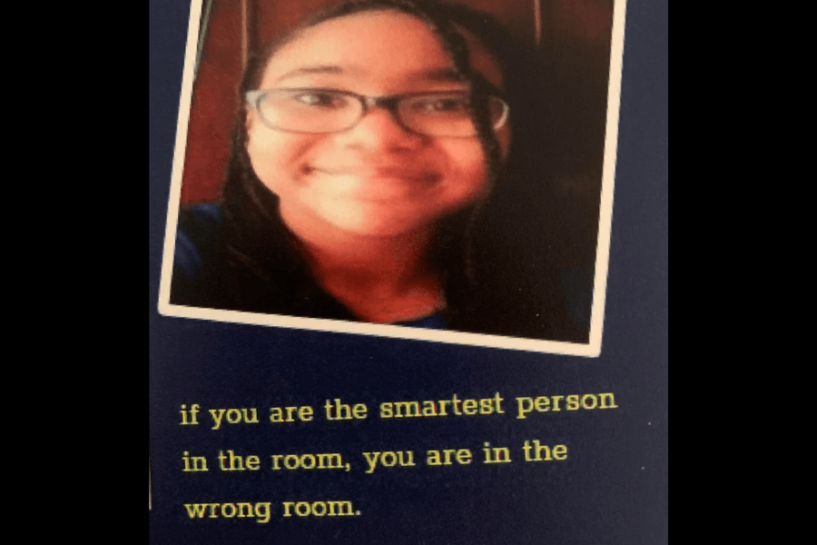  A yearbook photo of a young person wearing glasses and smiling at the camera, with a slightly tilted image frame on a dark blue background. Below the photo, their inspirational quote reads, "If you are the smartest person in the room, you are in the wrong room," encouraging continuous learning and growth.