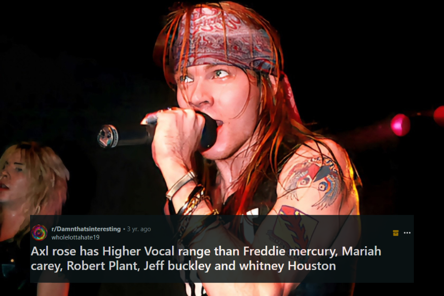 A male rock singer grips a microphone tightly, singing passionately on stage while wearing a red bandana over his long, flowing hair. His muscular arms, adorned with tattoos, are highlighted under the stage lights, exuding raw energy. The dark background with a partially visible band member adds to the intensity of the live performance.