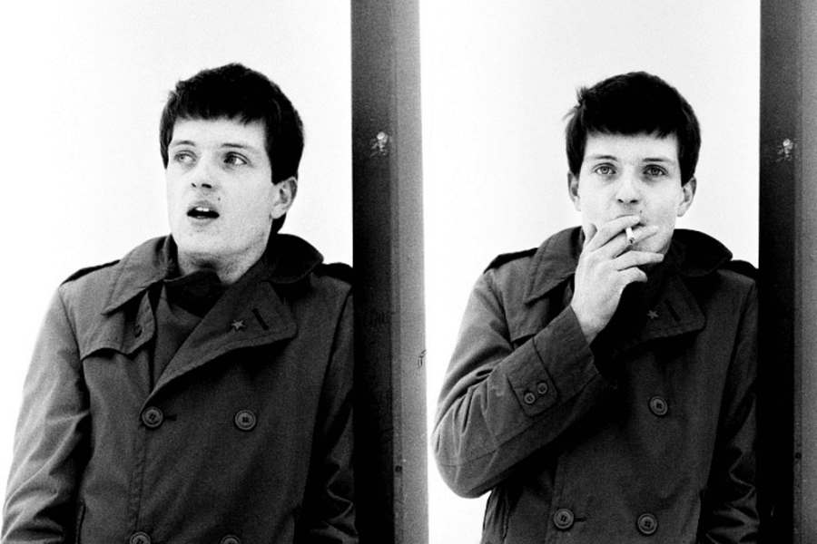 A black-and-white diptych photograph of a young man in a trench coat, separated by a vertical bar. In the left frame, he looks to the side with a slightly open mouth, while in the right frame, he gazes directly into the camera while smoking a cigarette. The stark contrast and minimalist background emphasize his expressions and mood.