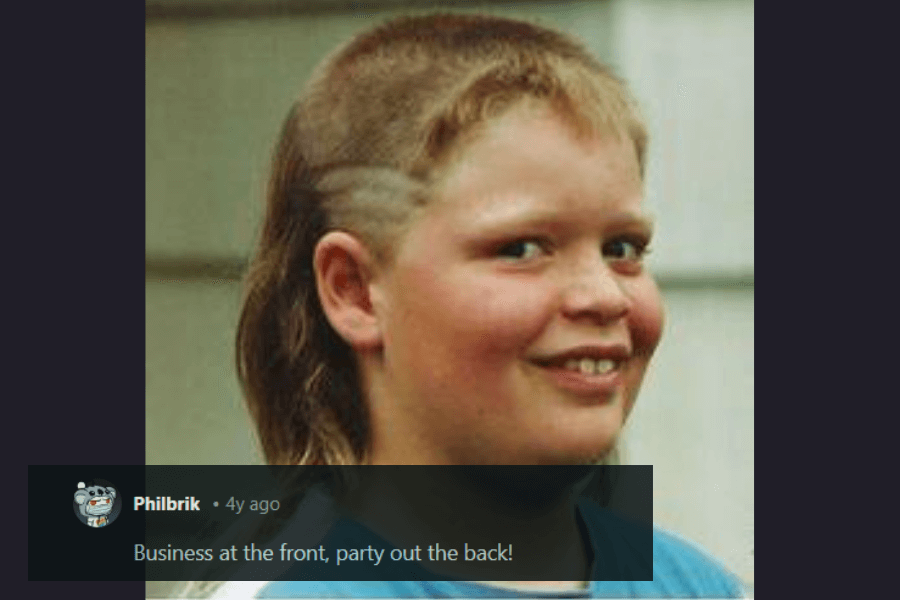 A young boy with a bold mullet hairstyle featuring shaved designs on the sides, short cropped hair on top, and long flowing locks in the back. He has a mischievous grin and is wearing a blue shirt, looking off to the side. The caption underneath humorously states, "Business at the front, party out the back!"