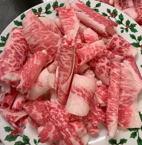 A plate with a festive holly design holds a generous portion of thinly sliced, marbled beef. The meat's rich red color contrasts with intricate white fat marbling, creating a visually striking texture.