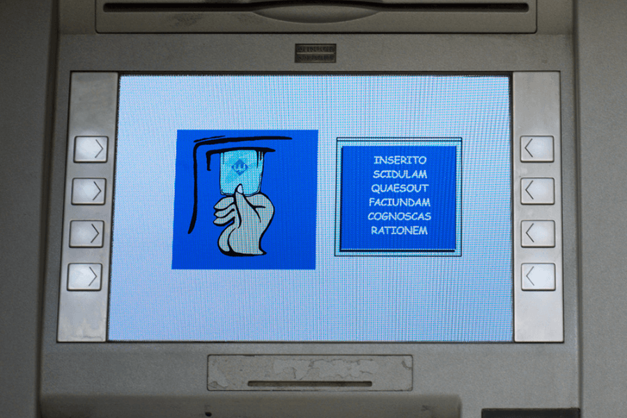 Close-up of an ATM screen displaying an illustration of a hand inserting a card and Latin placeholder text that reads “INSERITO SCIDULAM QUAESO UT FACIUNDAM COGNOSCAS RATIONEM.” The interface has navigation buttons on both sides of the screen.