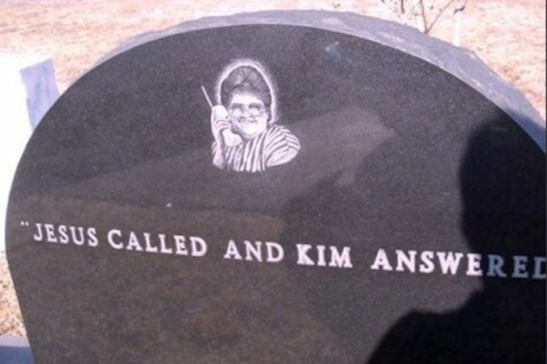 Black tombstone with a humorous engraving of a smiling woman holding a large cordless phone. The epitaph reads, “JESUS CALLED AND KIM ANSWERED,” implying a lighthearted take on her passing.