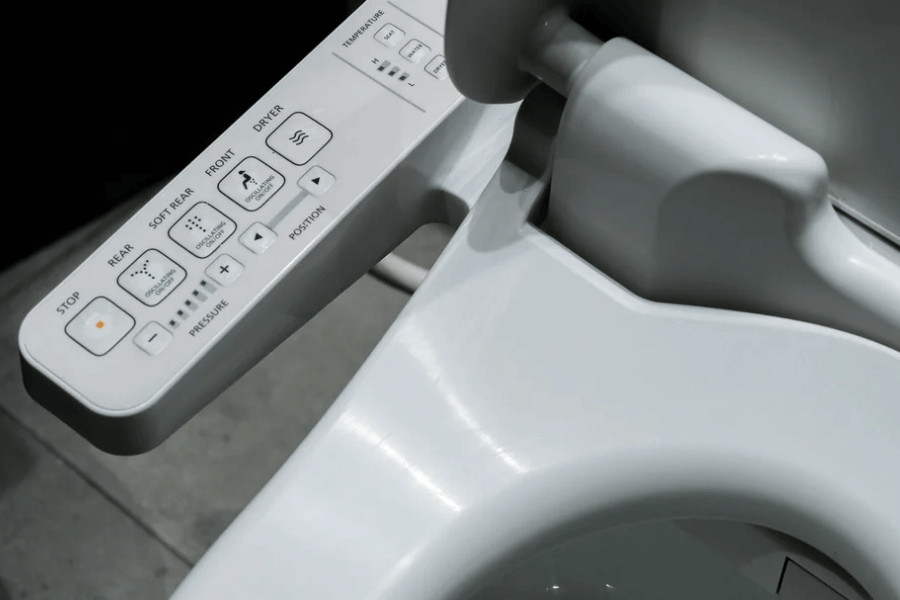 Close-up of a high-tech toilet bidet control panel, featuring buttons for rear and front cleansing, drying, temperature adjustment, pressure control, and nozzle positioning. The sleek white design highlights its modern, automated functionality.
