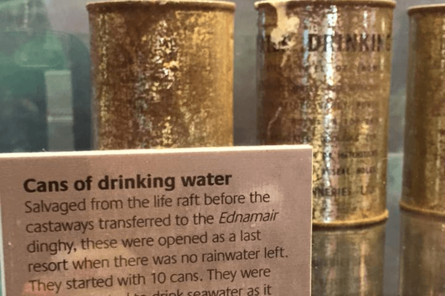 Close-up photo of a museum display showing rusted cans labeled “Drinking Water” behind a sign. The sign explains that the cans were salvaged from a life raft before castaways moved to the Ednamair dinghy, and were used as a last resort when rainwater ran out.