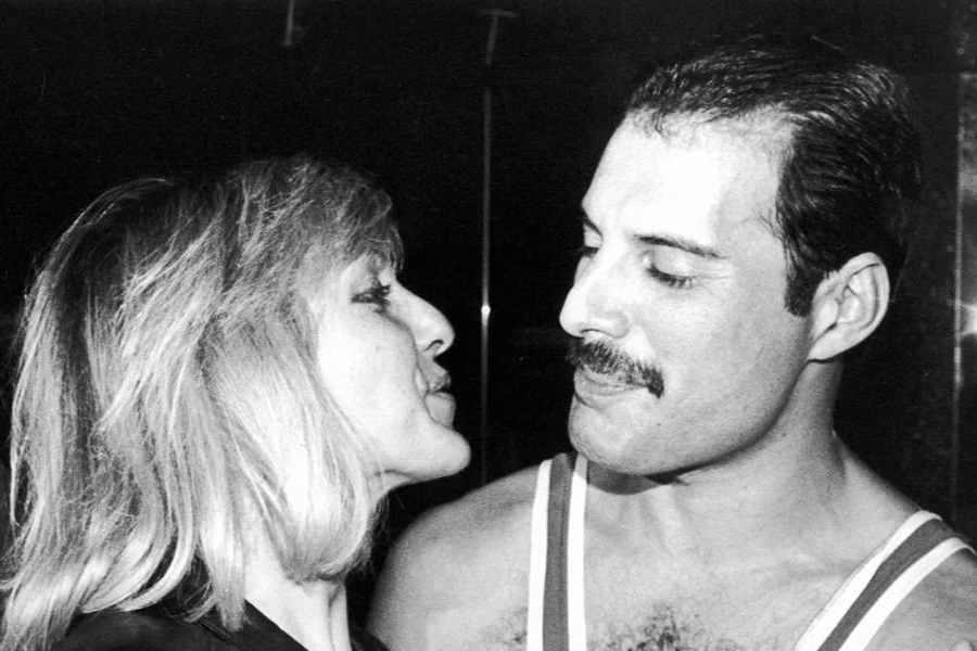 Black and white close-up photo of Freddie Mercury gazing affectionately at Mary Austin, who faces him with a soft expression. Freddie wears a tank top and has a slight smile, while Mary leans in closely, capturing a tender moment between the lifelong friends.