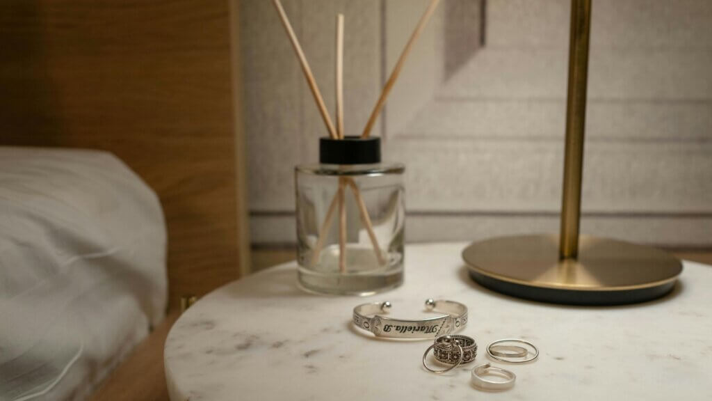 Rings, bracelet, and perfume bottle on a small table beside a bed