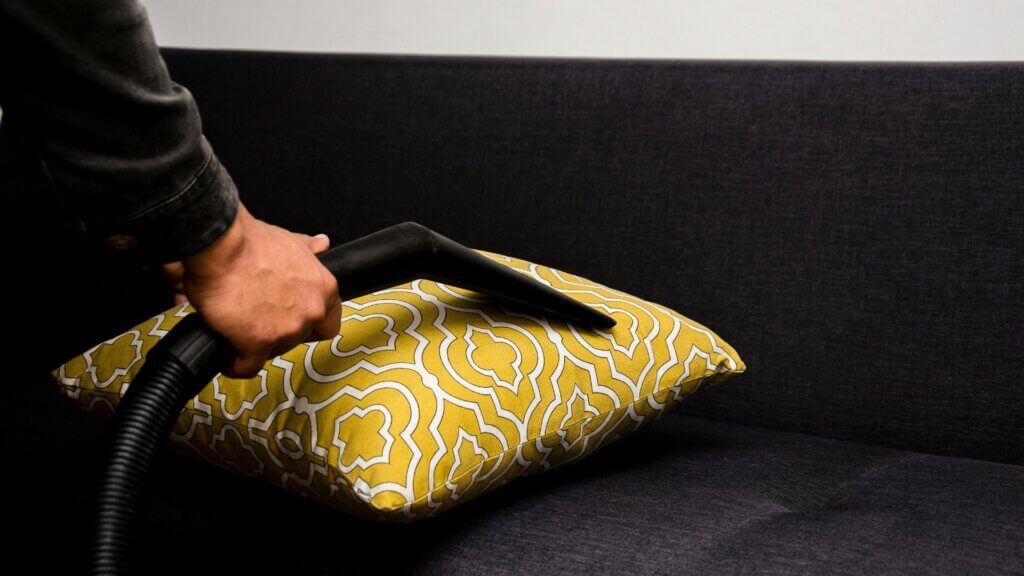 Person cleaning a beige throw pillow on a couch