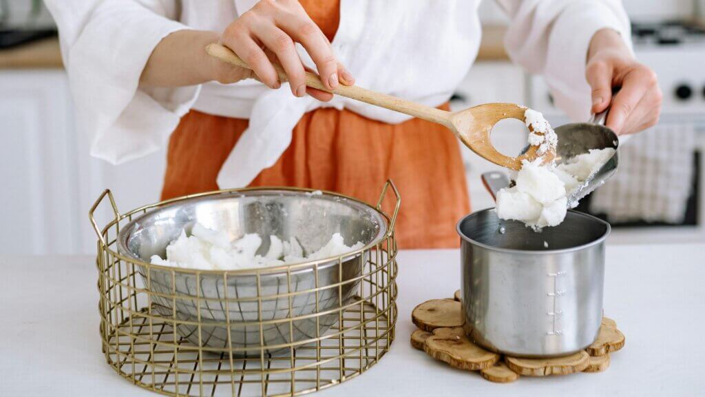 Woman placing candle wax into a stewpan in a kitchen