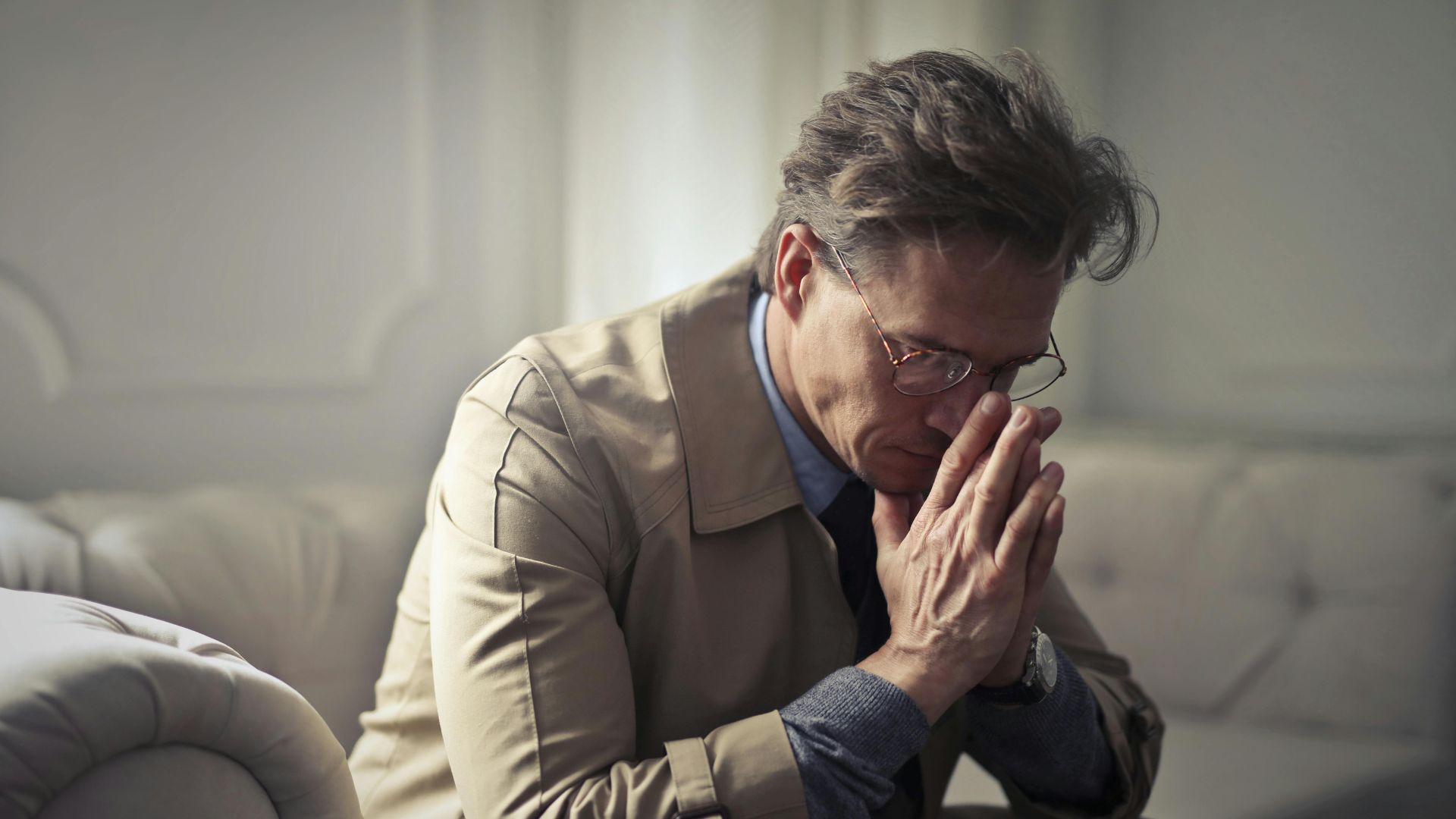 Sad mature businessman sitting in living room with hand on chin, looking concerned