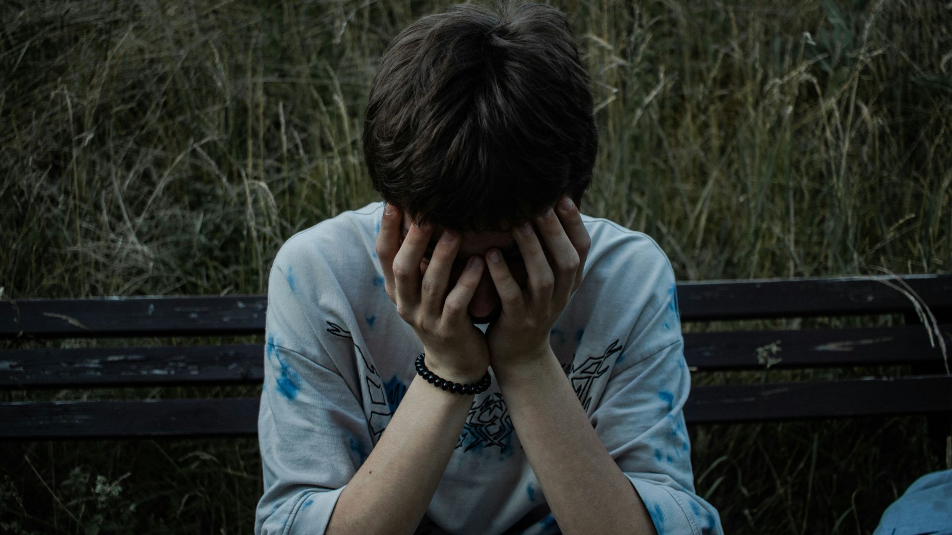 Person sitting on a bench with hands on face, looking worried