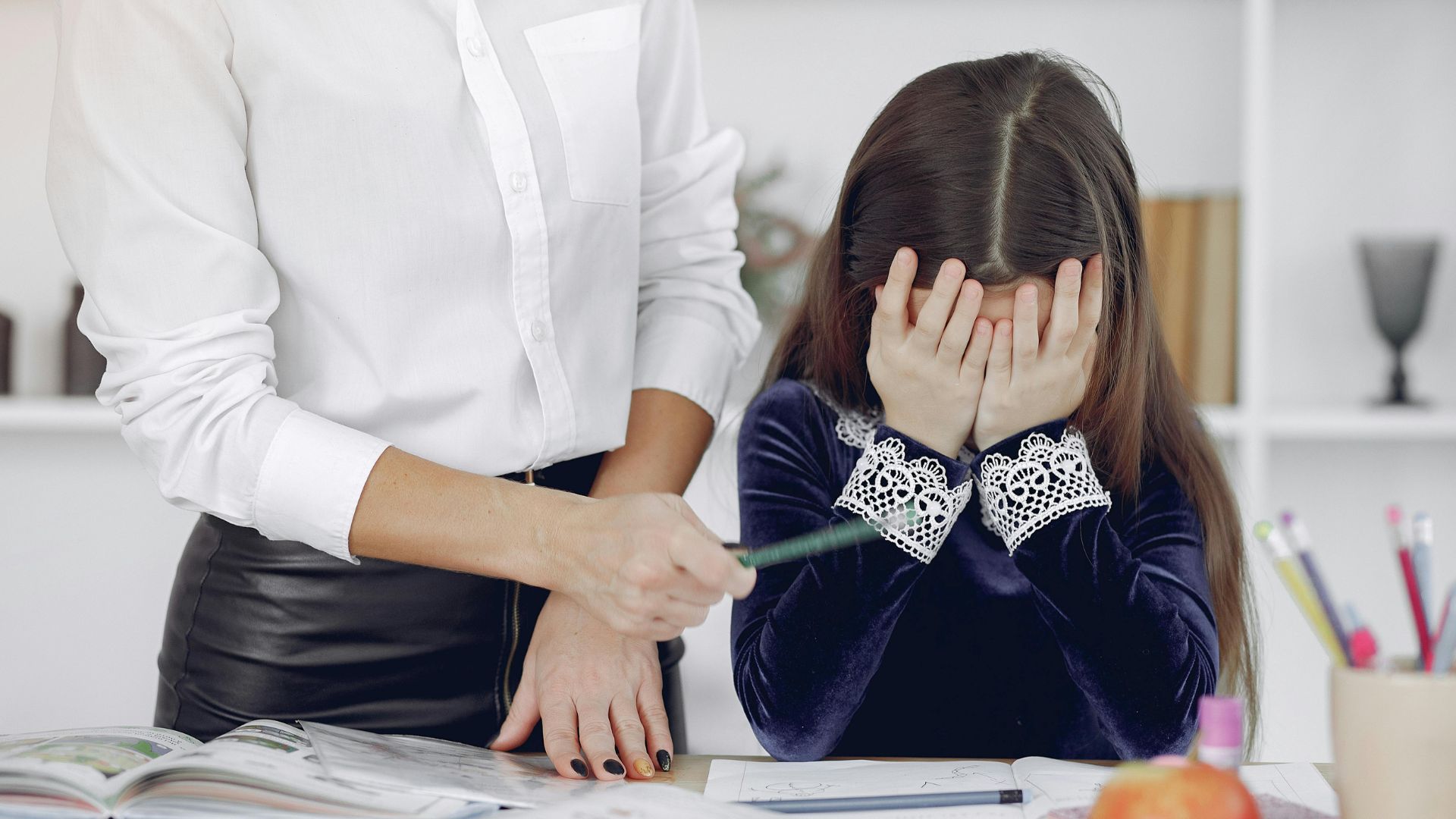 Upset little girl sitting near a woman in a classroom