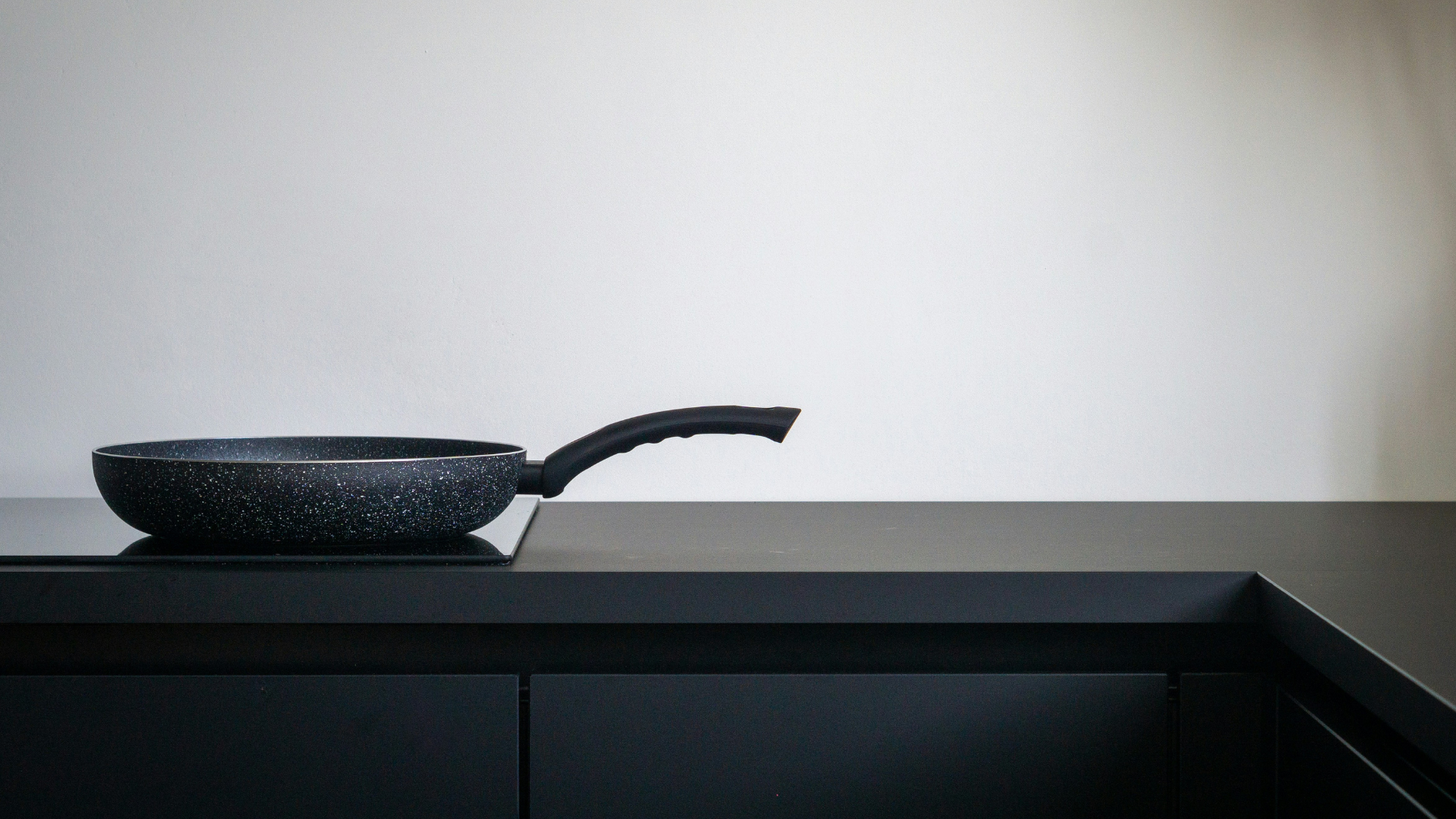 Black kitchen space with matte finishes and textured wood and leather details