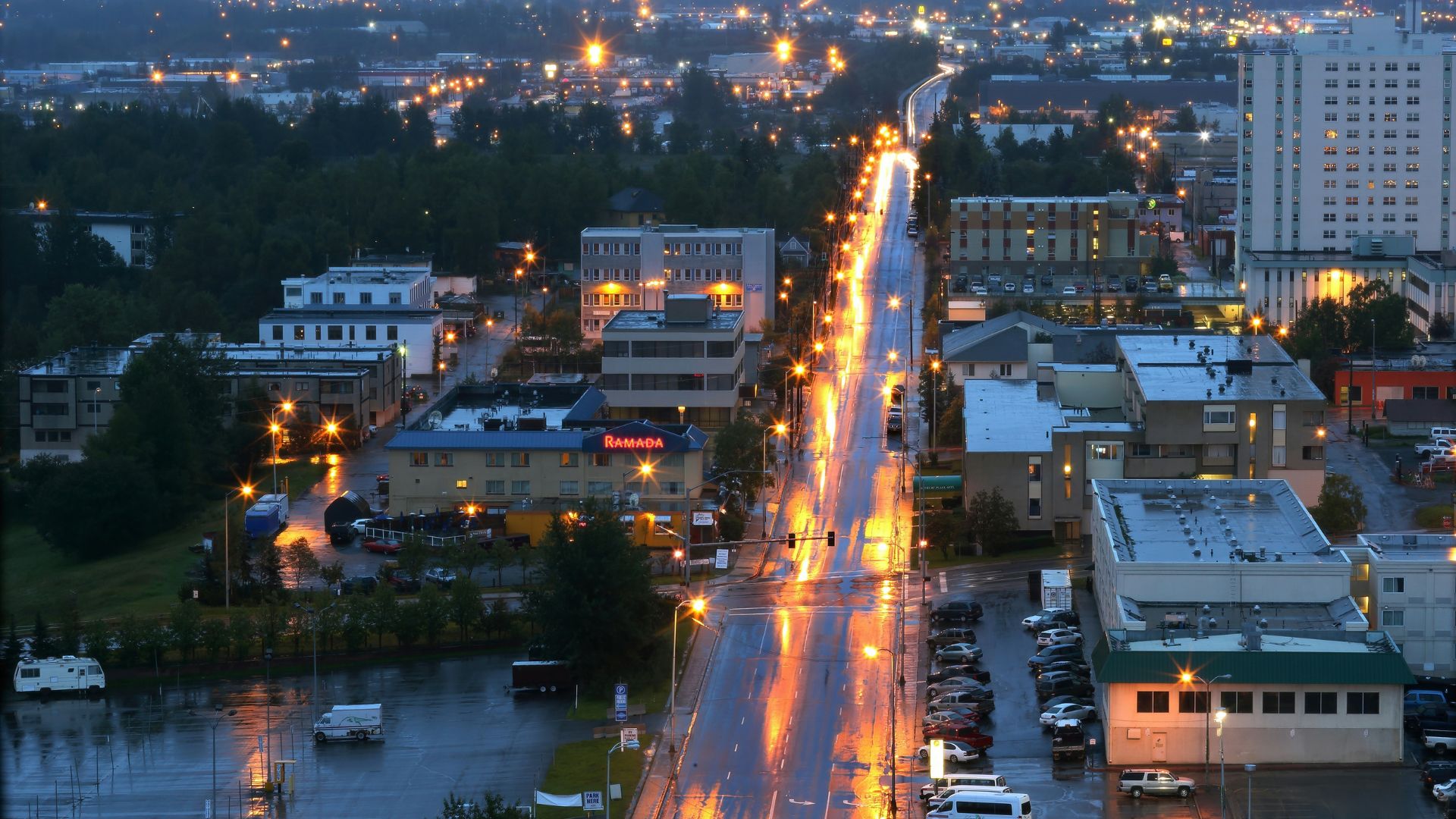 Cars driving on a road in Alaska during night with city lights in the distance