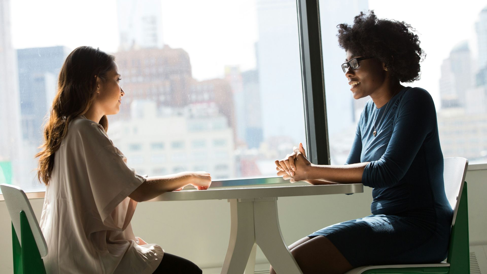 Two women sitting beside a table and talking