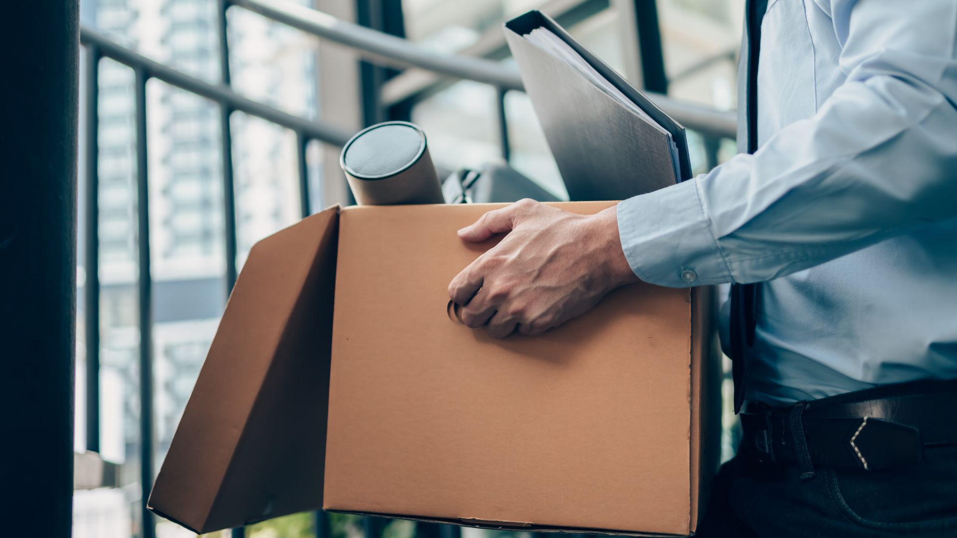 Unemployed worker holding a cardboard box and laptop bag after leaving workplace