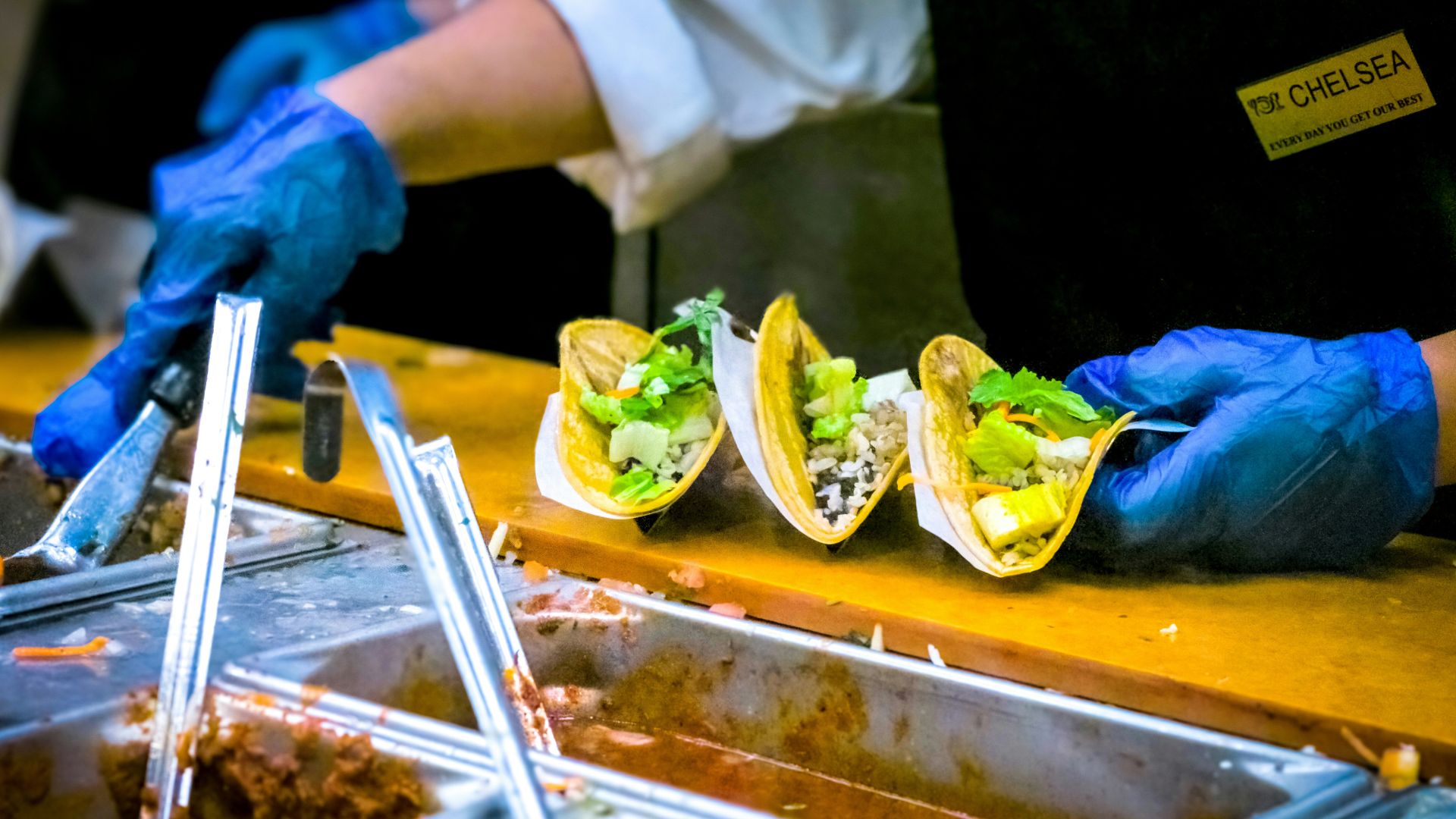Person preparing tacos with toppings and sauce