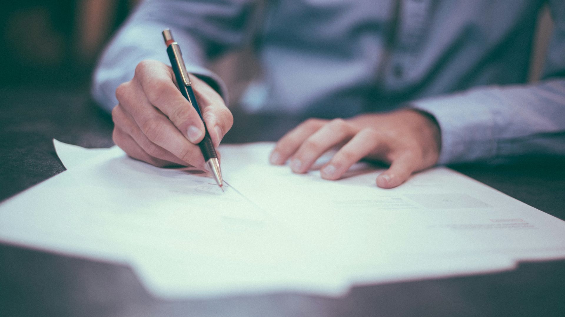 Man writing on paper at a desk with documents