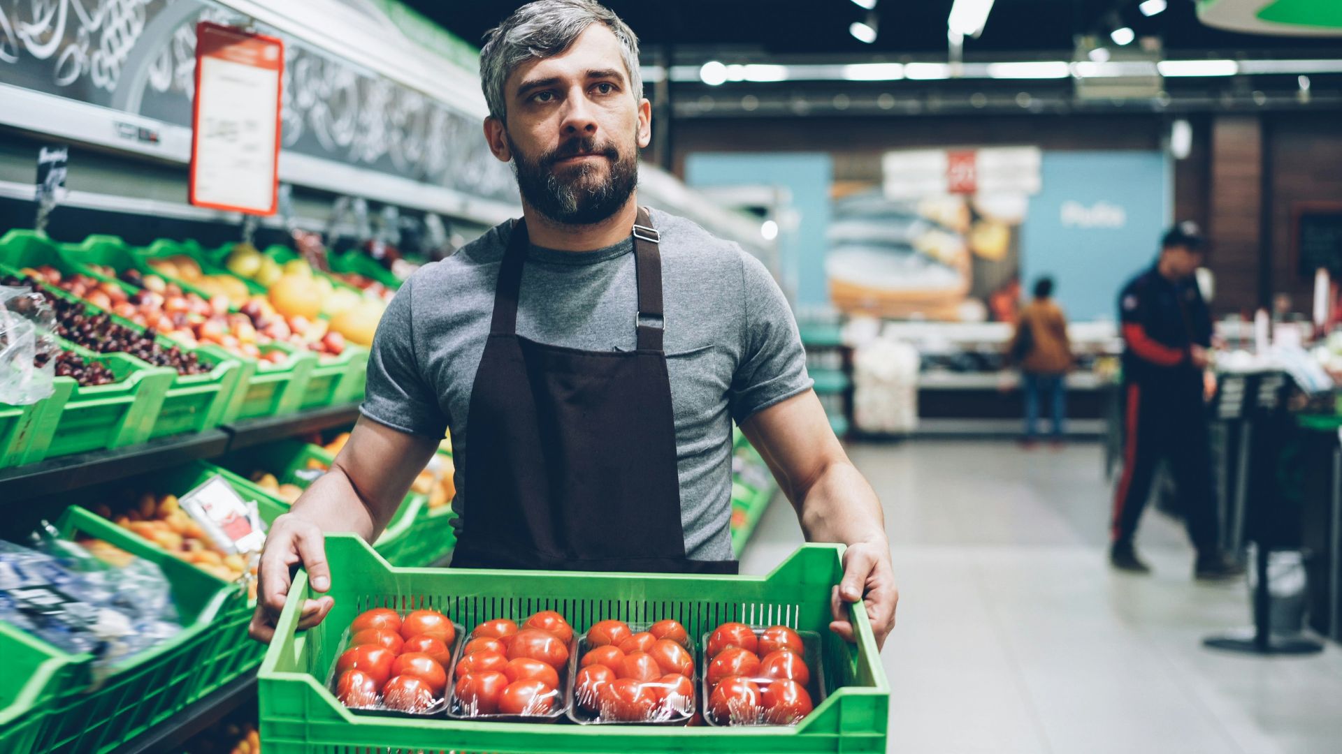 Grocery store worker holding a box of tomatoes