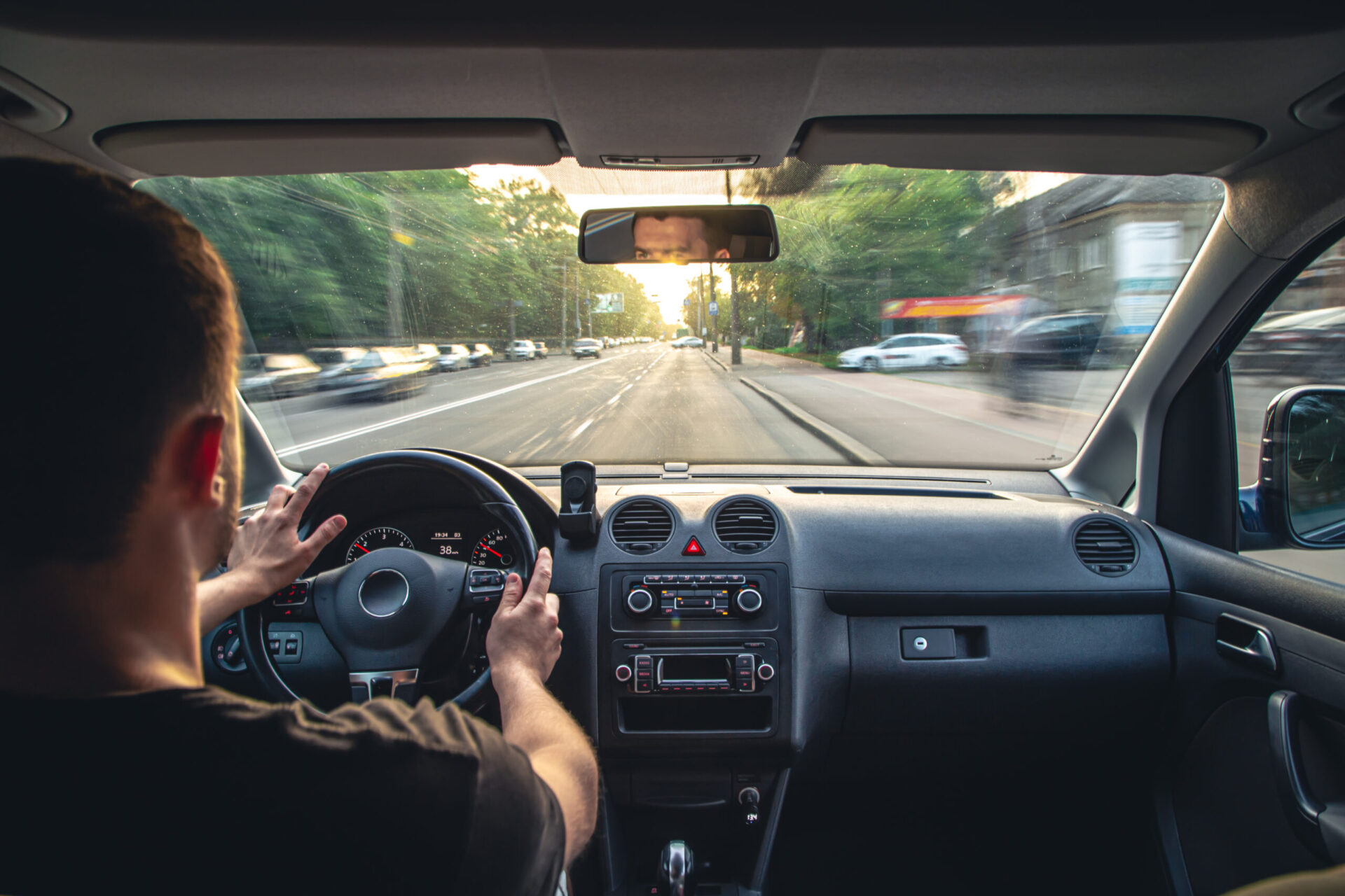 Driver’s view from inside a car with hands on the steering wheel while driving on a city street.