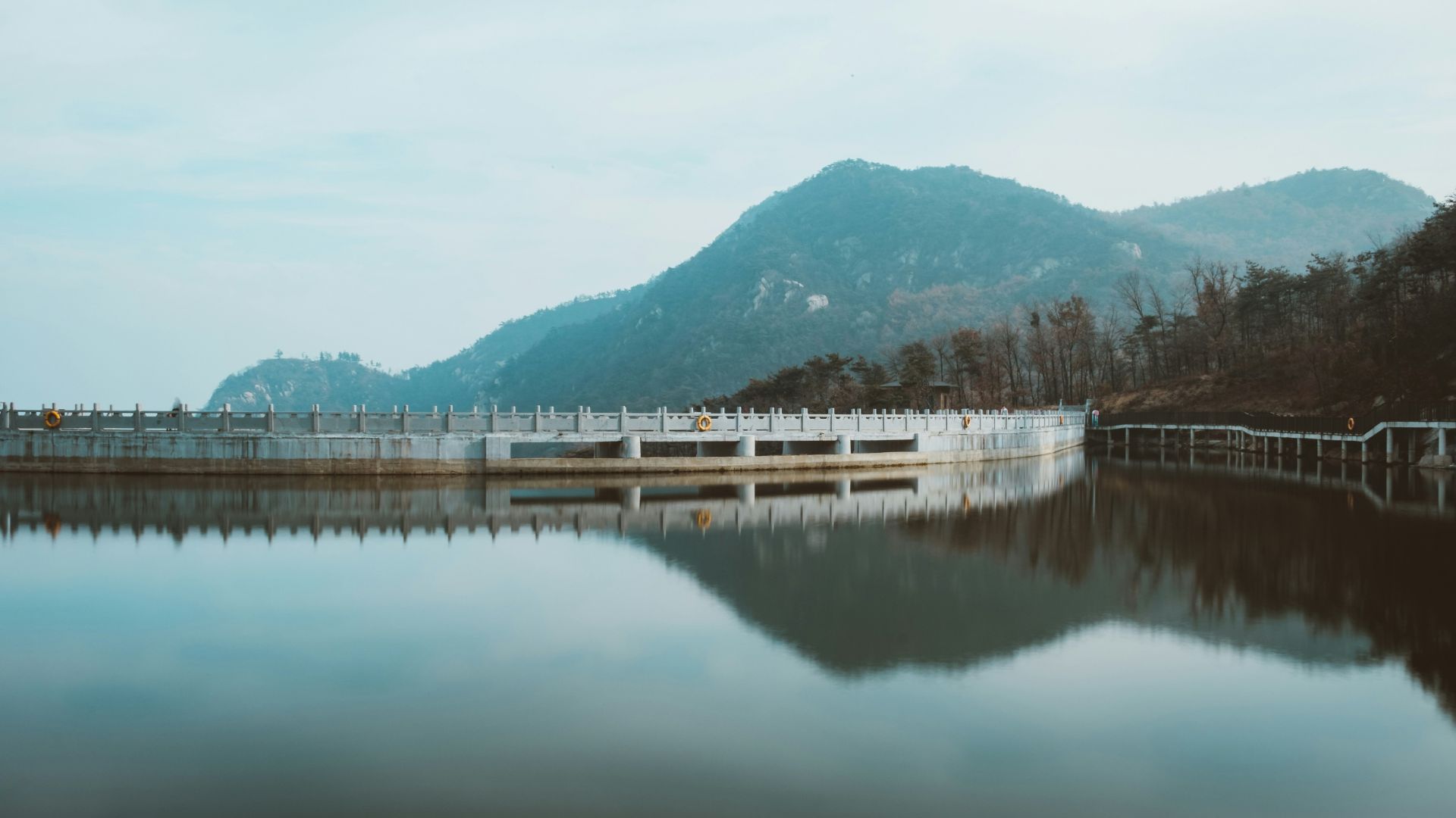 Wide dam filled with calm blue water beneath a clear sky