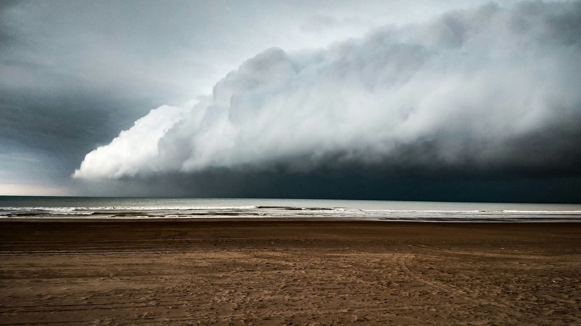 Large storm cloud hovering above a beach at sunset