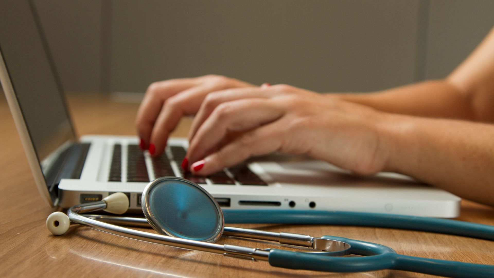 Person using a laptop with a stethoscope on a desk beside them