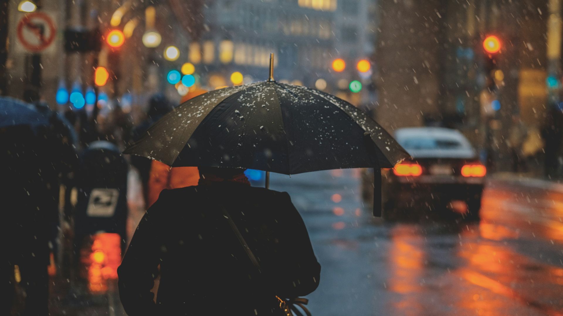 Person walking under an umbrella in heavy rain on a city street