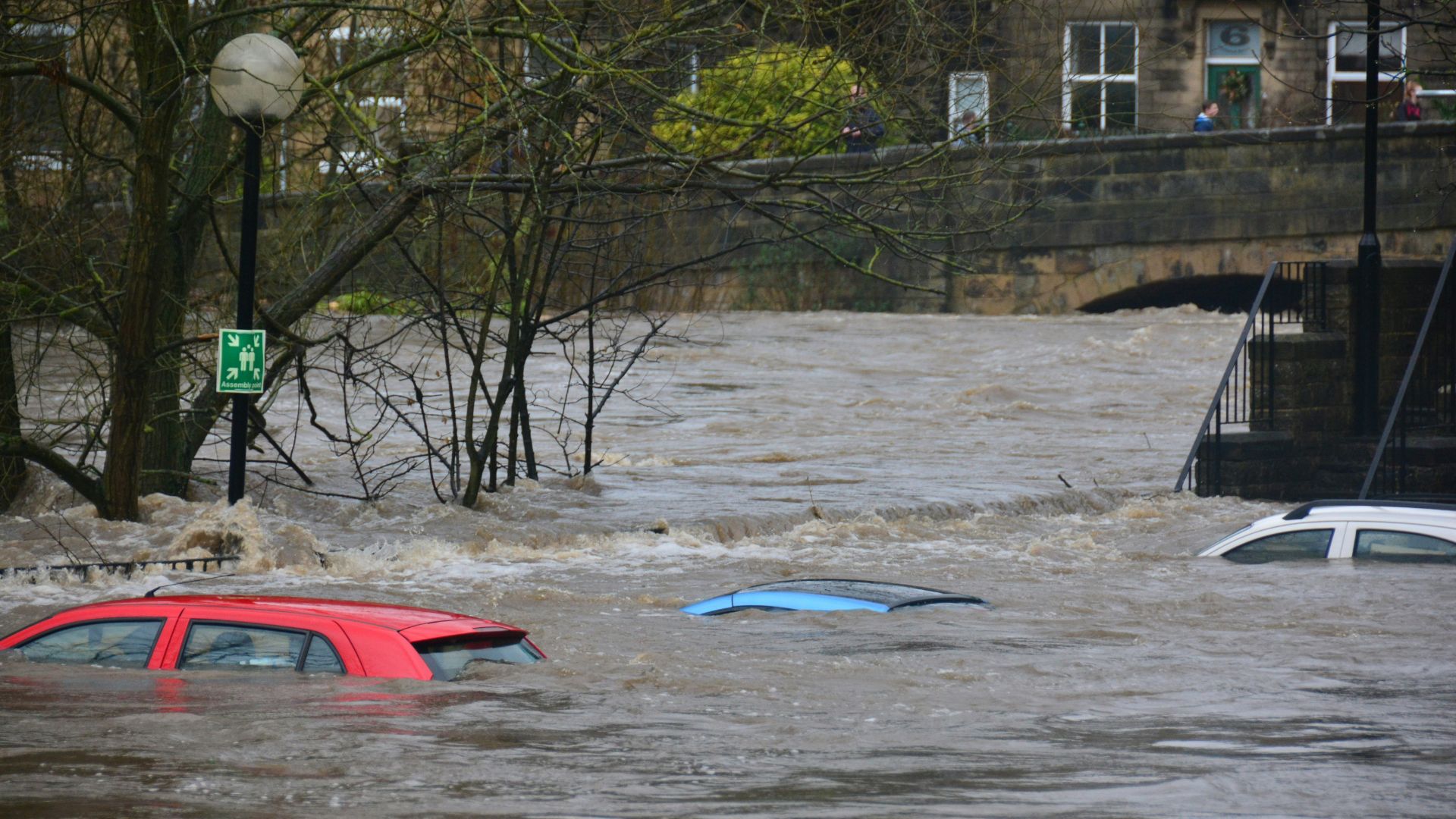 Blue car parked on a flooded coastal road with vast water stretching toward the horizon.