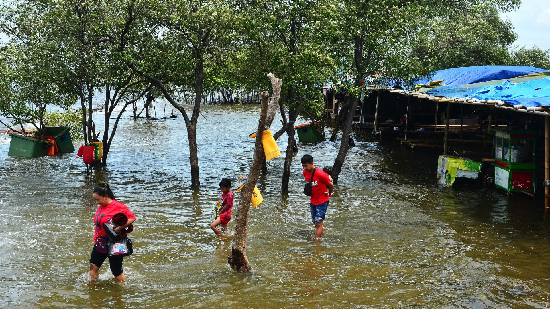 People carefully walk through ankle-deep water on a city street after heavy flooding.