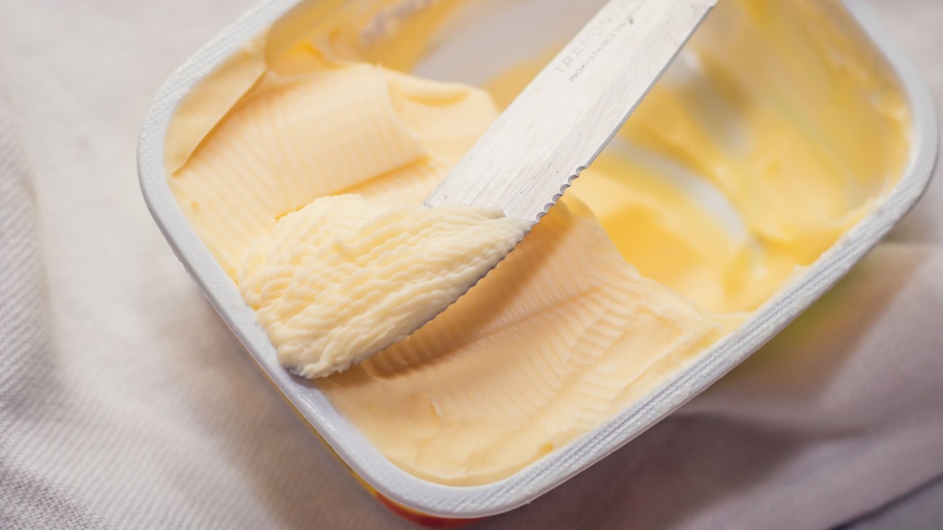 Person scooping margarine from a jar with a butter knife