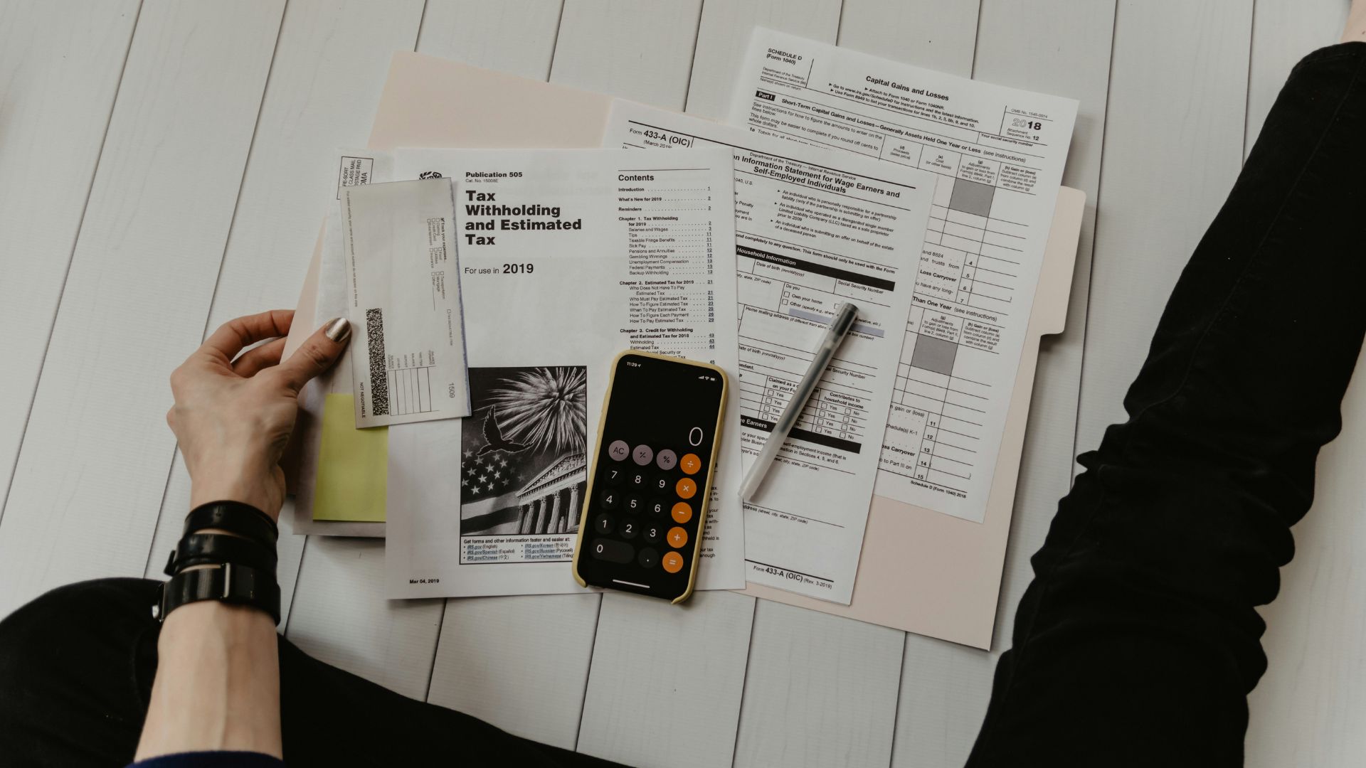 Person holding a paper and pen beside a calculator on a desk