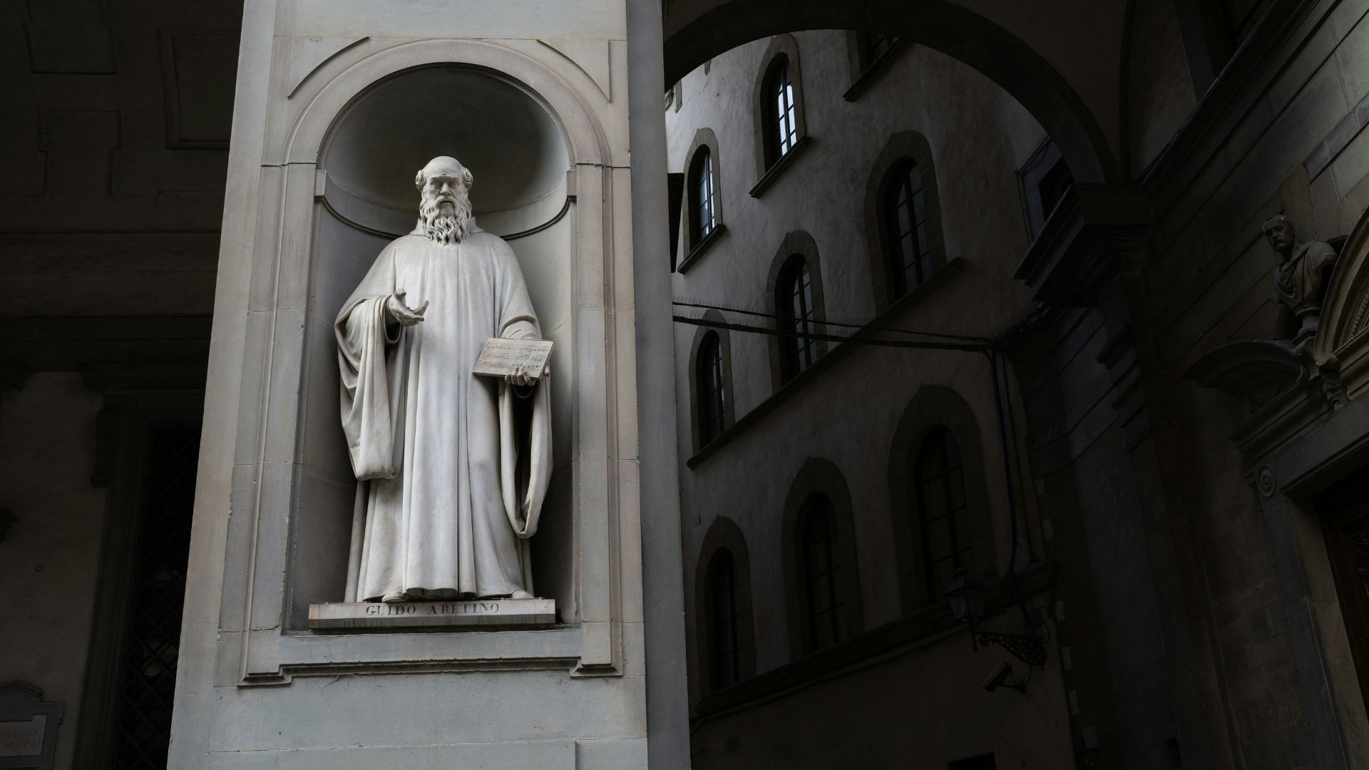 Stone statue of a man holding a book outside a large public building