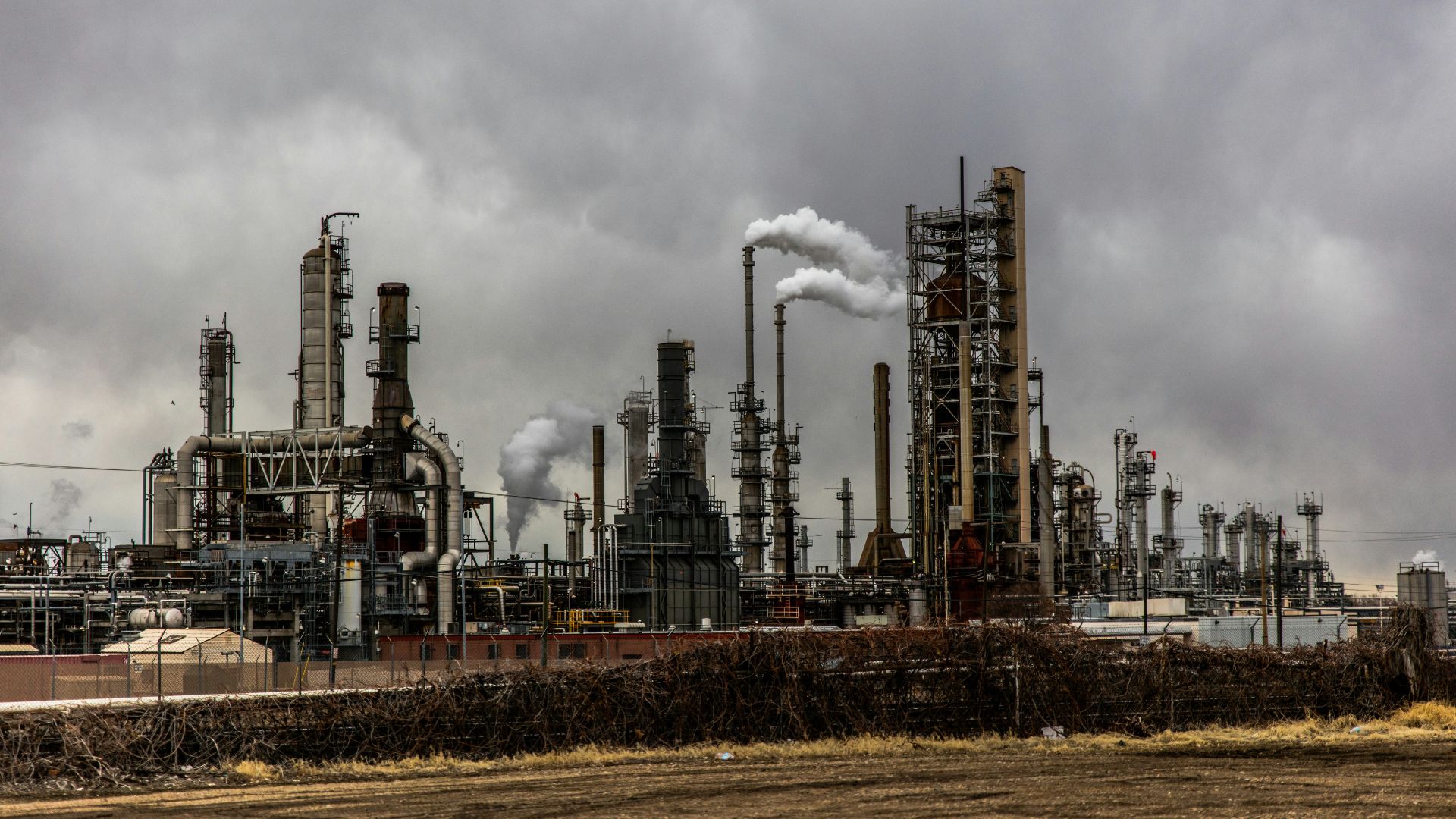 Several factory buildings with smoke rising into a cloudy sky