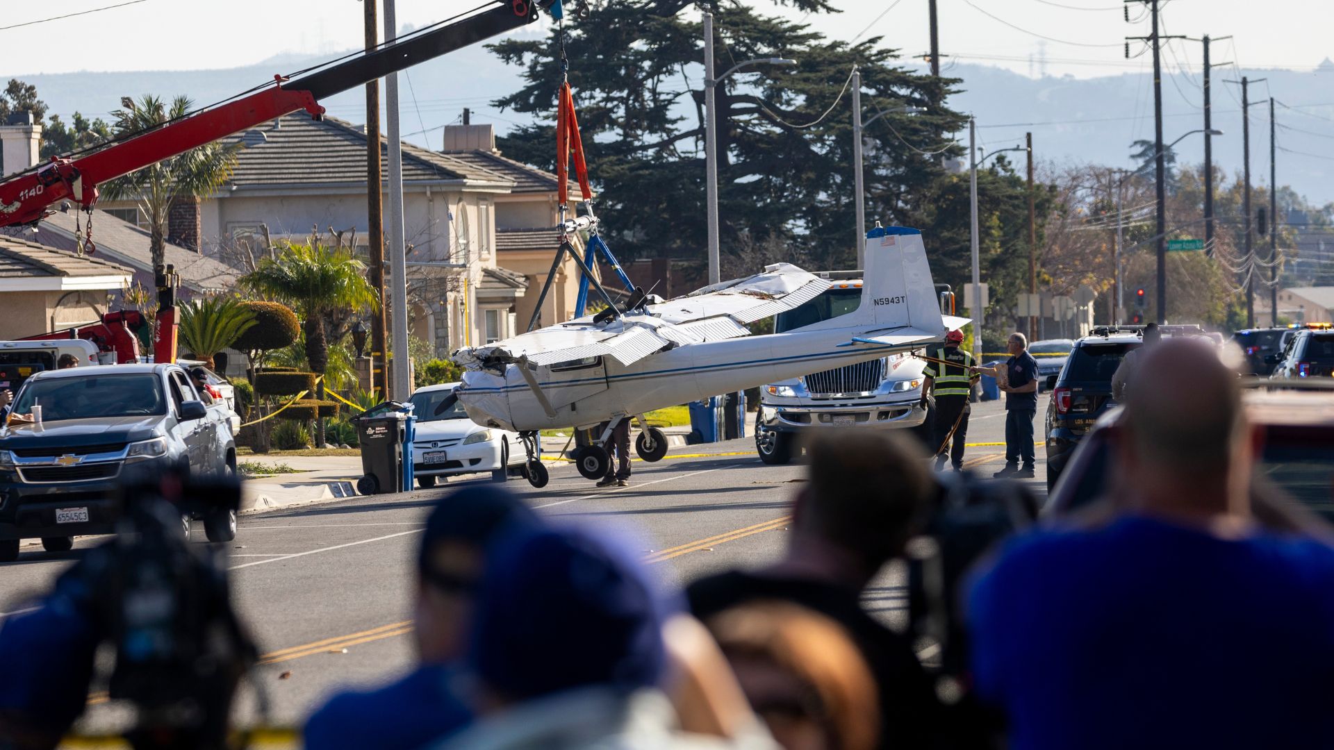 Workers using a crane to lift a damaged small airplane at a crash site near a runway