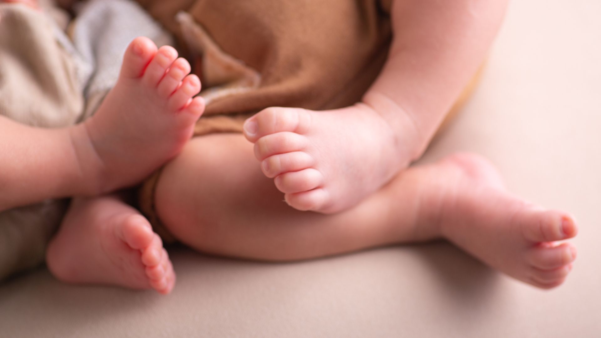 Newborn twins lying side by side with their feet touching