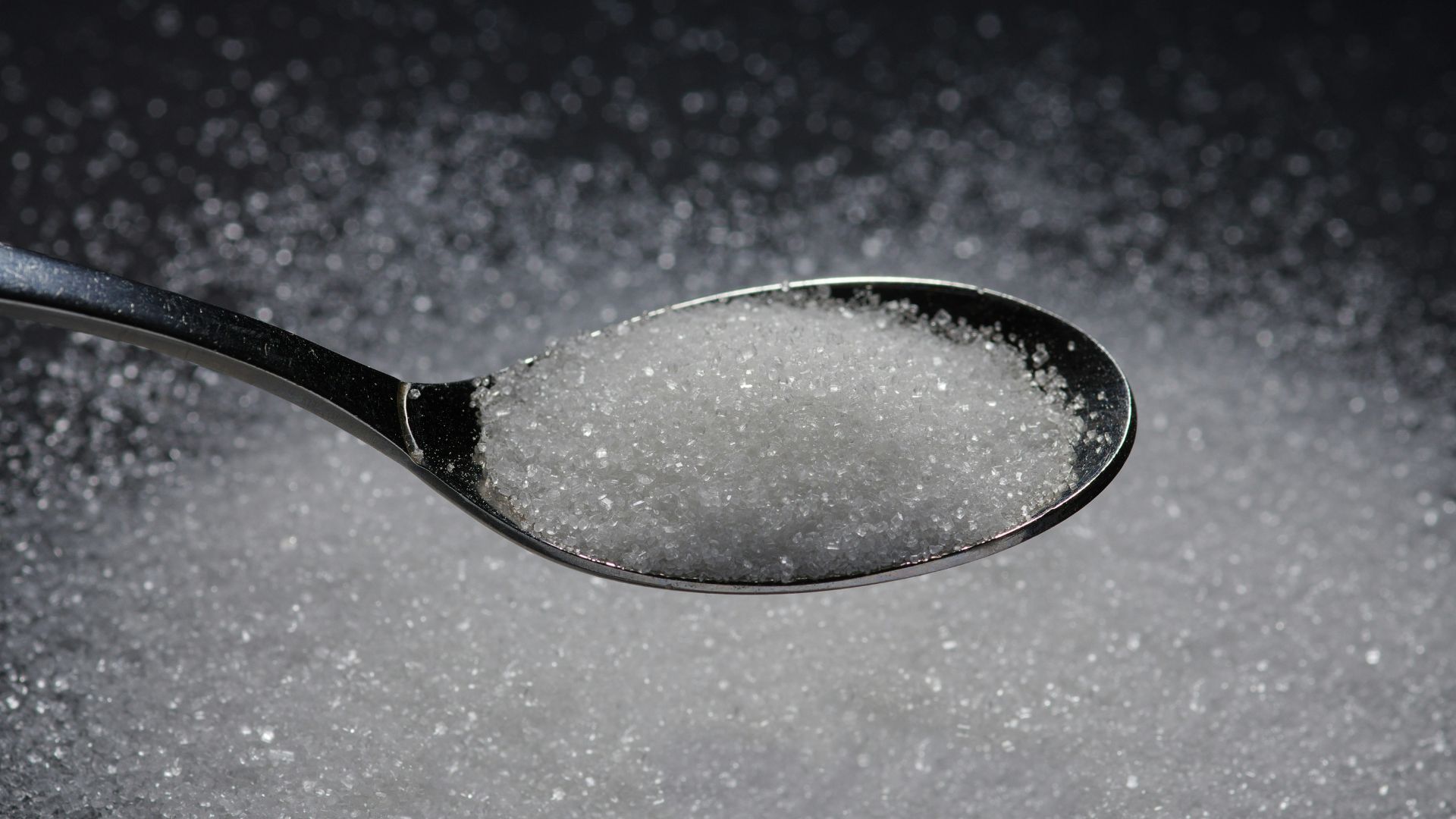 Close up of a spoon filled with sugar grains resting on a table