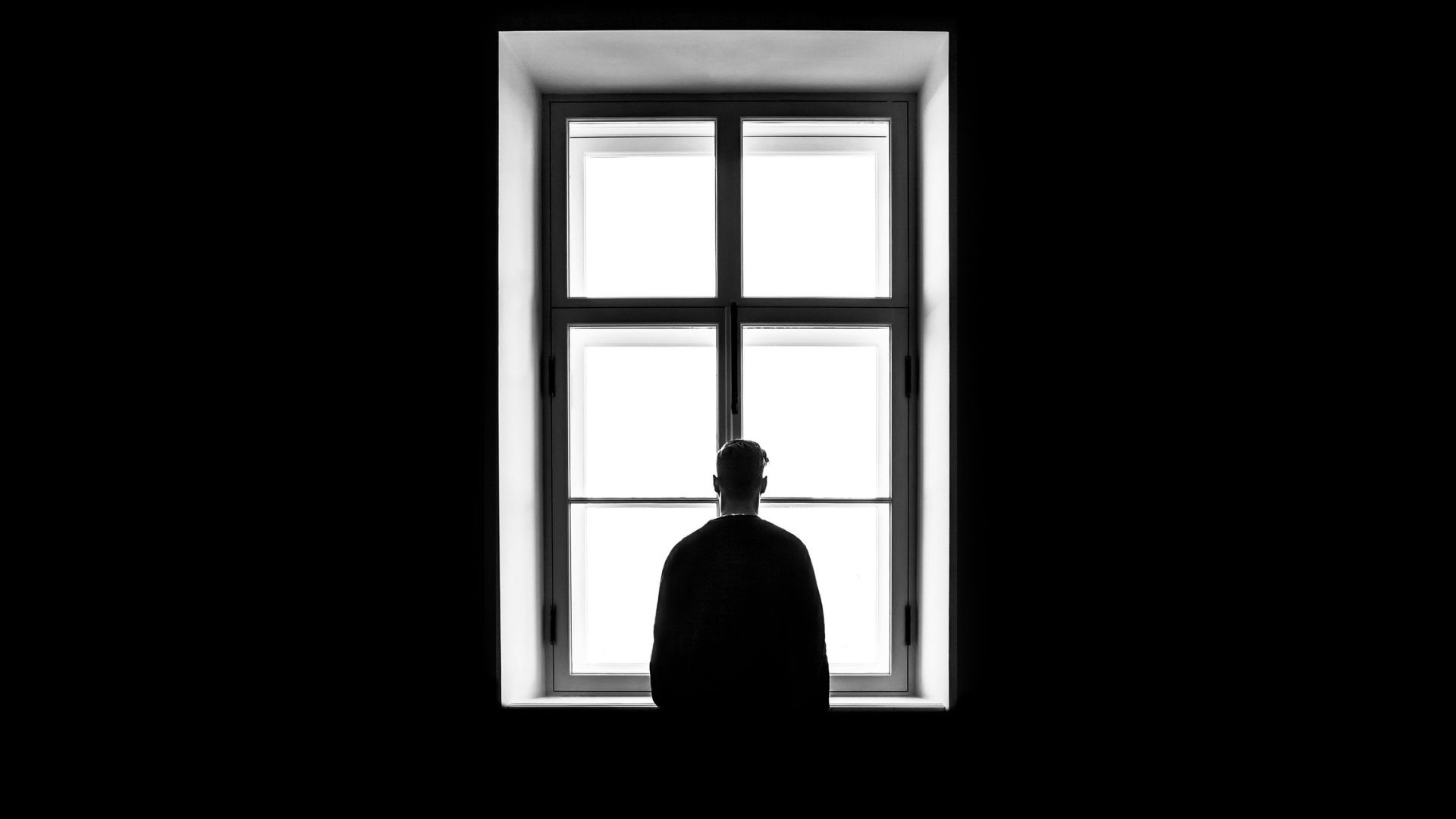 Man standing inside a dim room while looking through a large window