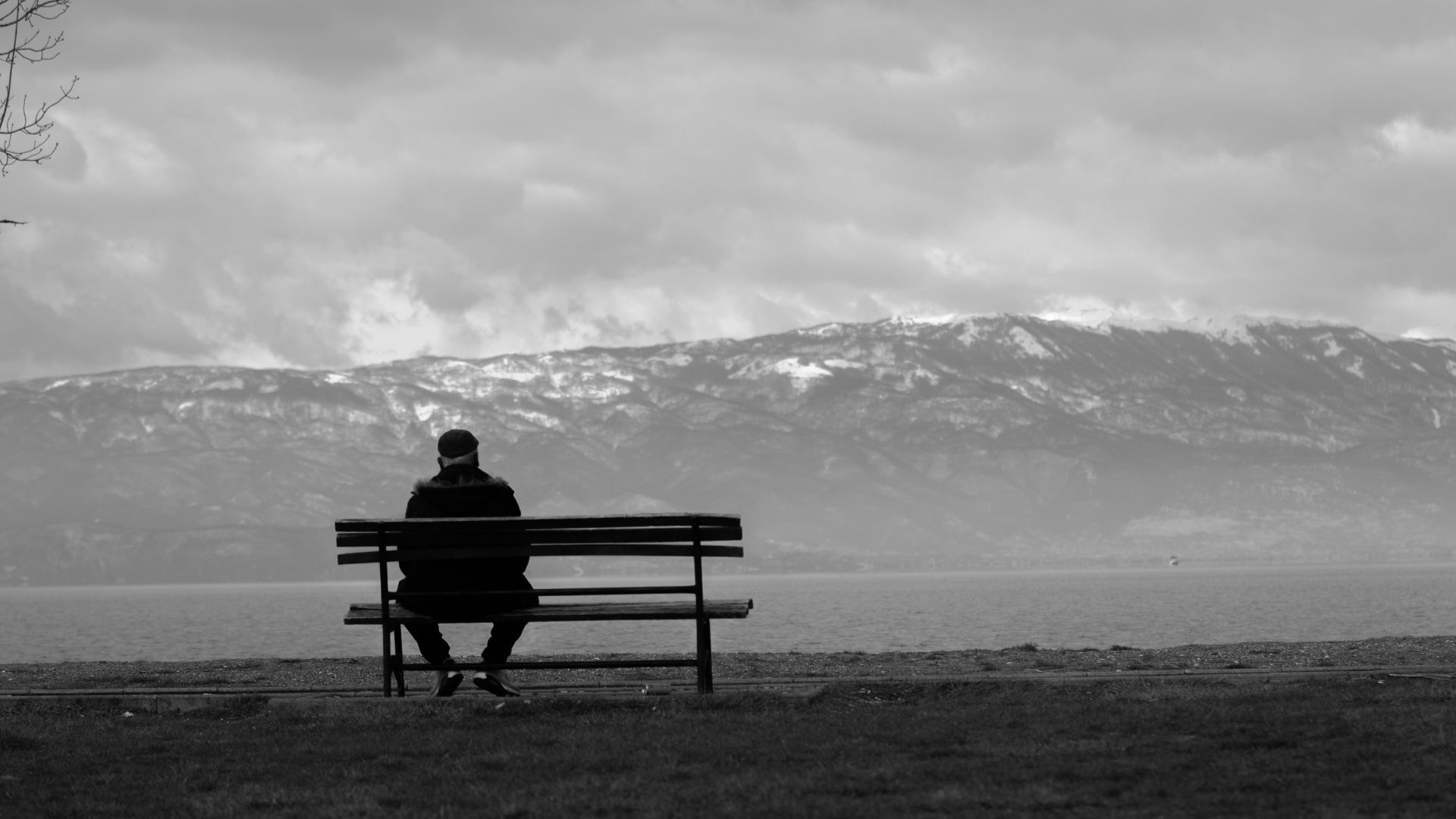 Grayscale image of a man sitting alone on a bench in an empty park