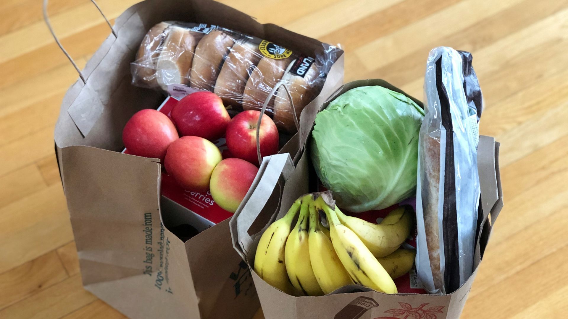 Cardboard box filled with apples and bananas in a grocery setting.
