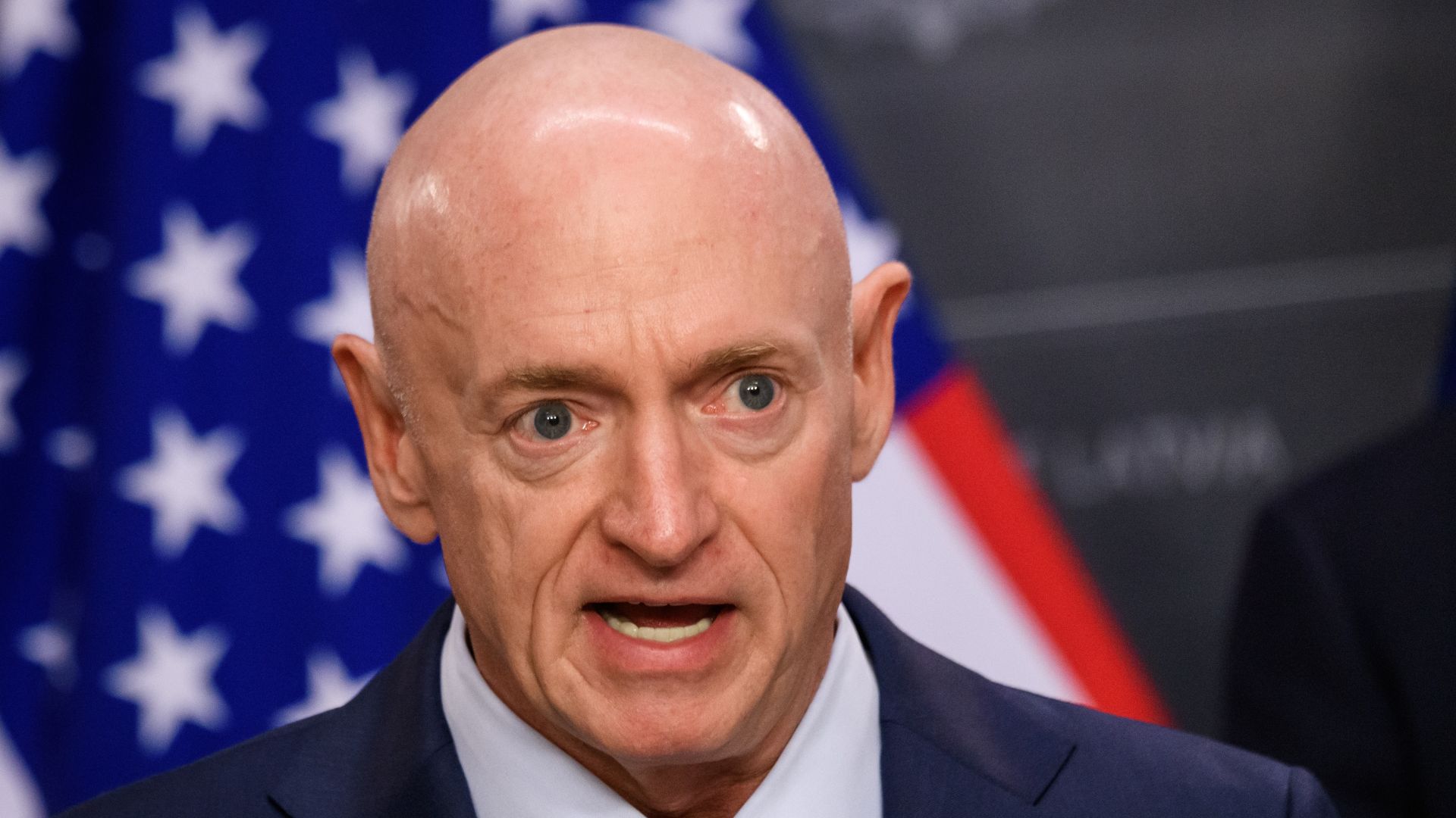 Mark Kelly speaking at an event in Riga with a microphone in hand