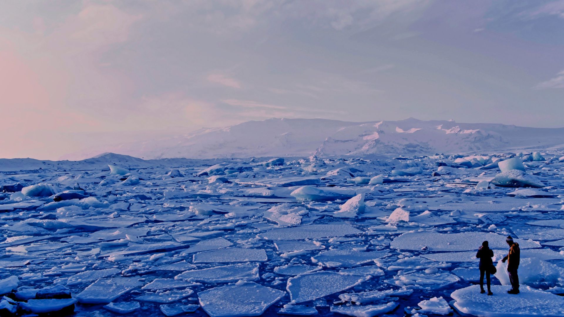 Two people standing on cracked sea ice under a gray cloudy sky
