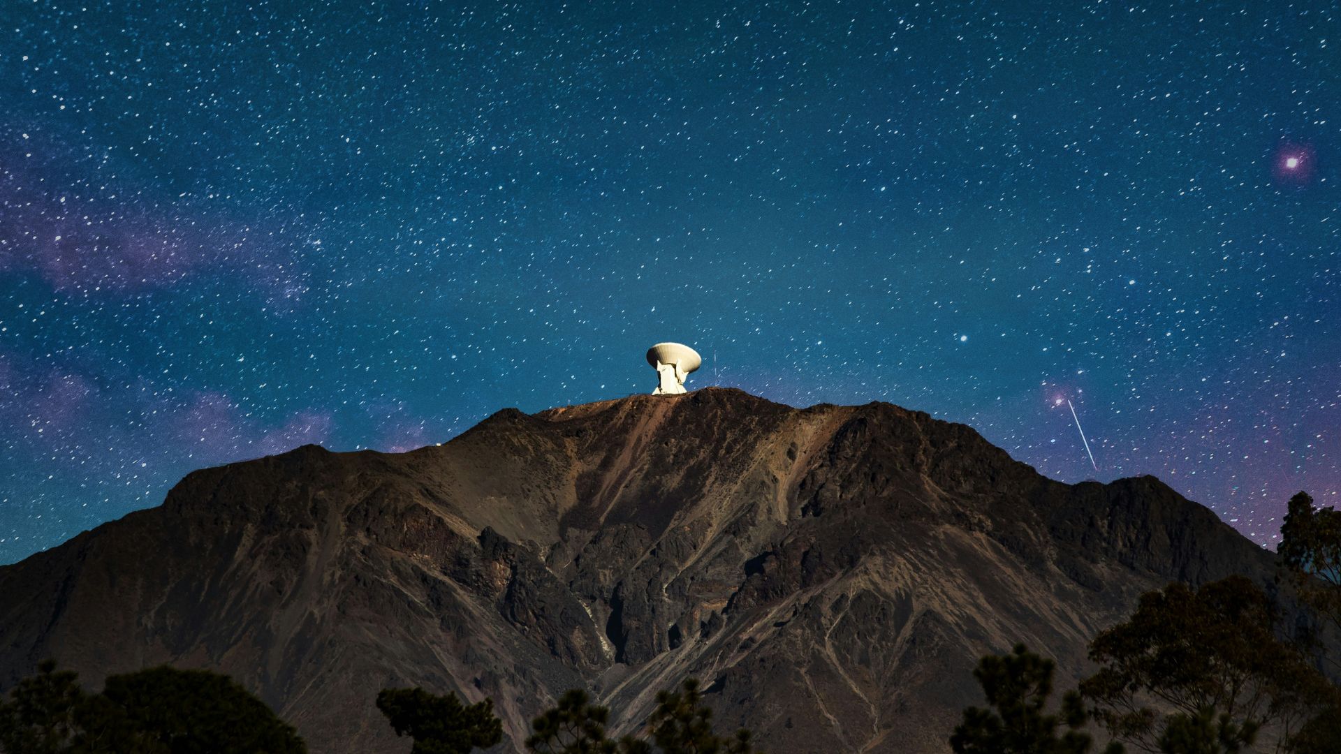 Satellite standing on a mountain peak during nighttime with stars behind it